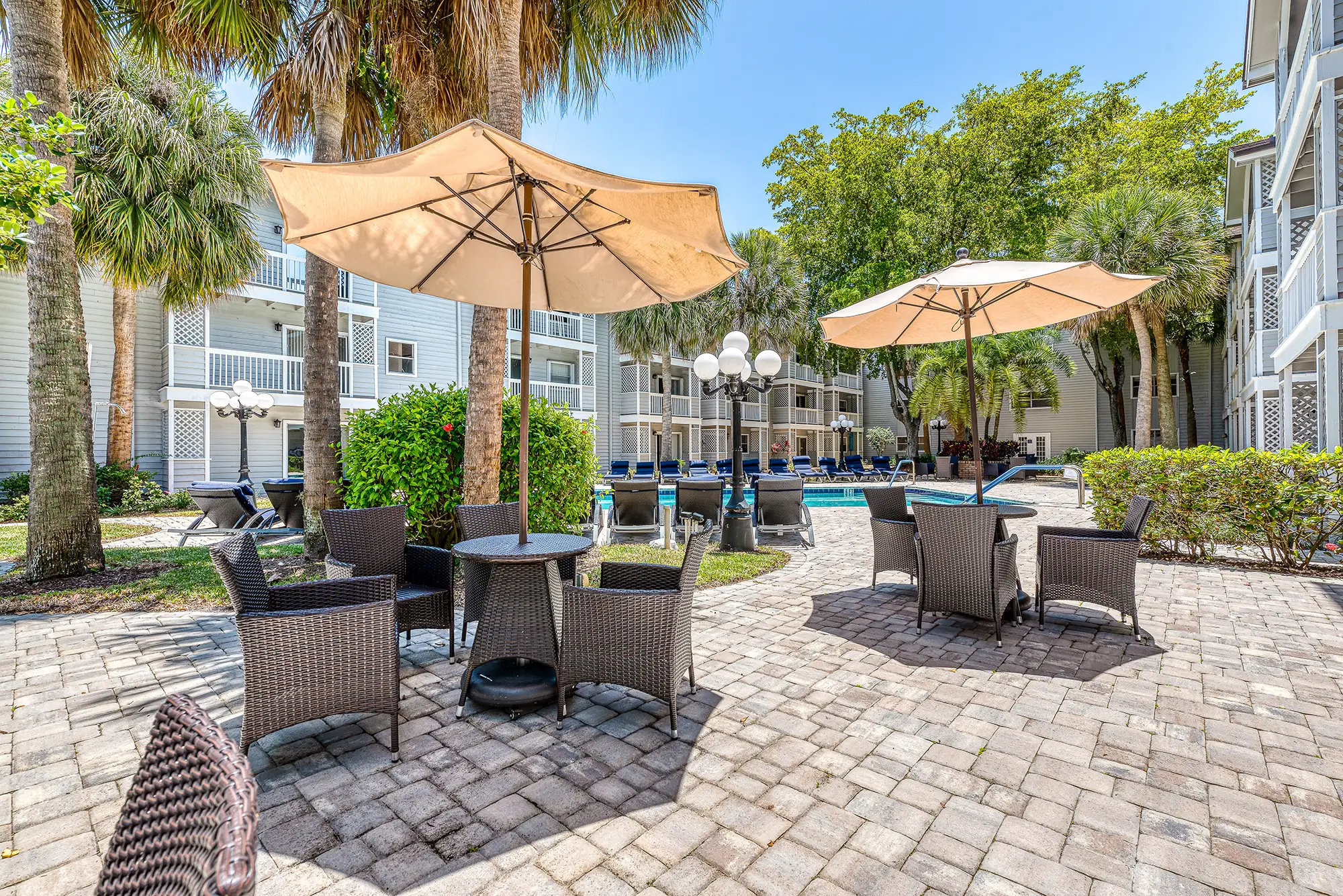 An exterior view of 3 tables with 11 chairs and two umbrellas outside of  a 55+ apartment senior living community